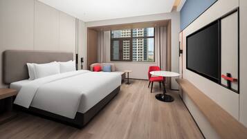 Una habitación de hotel moderna con una cama grande, una mesita pequeña, una silla roja y un televisor.