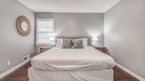 A bedroom with a large bed, two bedside tables, a window with blinds, a wall-mounted mirror, and a ceiling with a textured finish. - Shelby Parks Farm Haddington Home (Memphis)