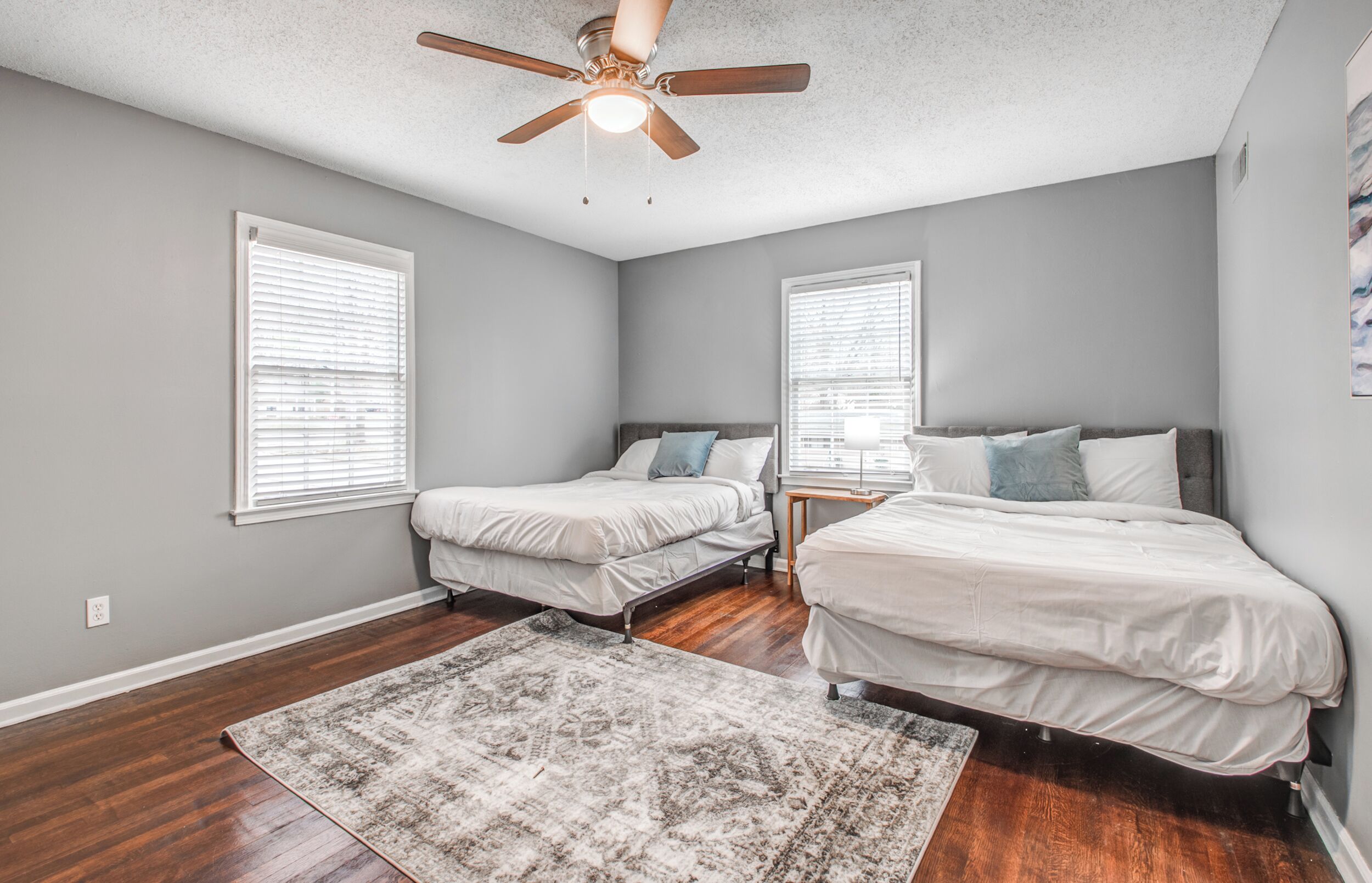 A bedroom with two single beds, a ceiling fan, and a patterned rug.