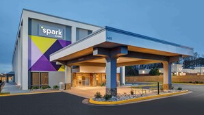 Un hotel moderno con fachada geométrica, acceso cubierto y zona de estacionamiento bien iluminada.
