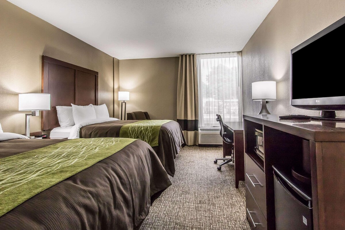 A hotel room with two beds, a desk, a television, and a window with curtains.