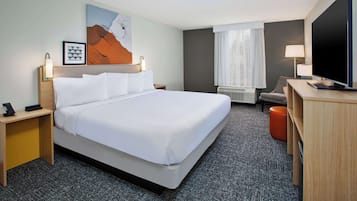 A hotel room with a large bed, a desk with a TV, a chair, a lamp, and artwork on the wall.