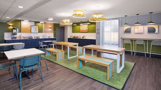 Un café moderno con mesas de madera y sillas azules, paredes verdes y luces de techo.