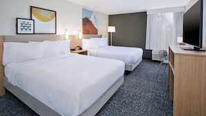 Habitación de hotel con dos camas, un escritorio, un televisor y una ventana con cortinas.