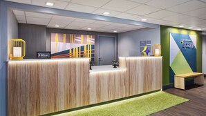 Un mostrador de recepción de hotel con diseño moderno, alfombra verde y un letrero de 'Hilton Honors'.
