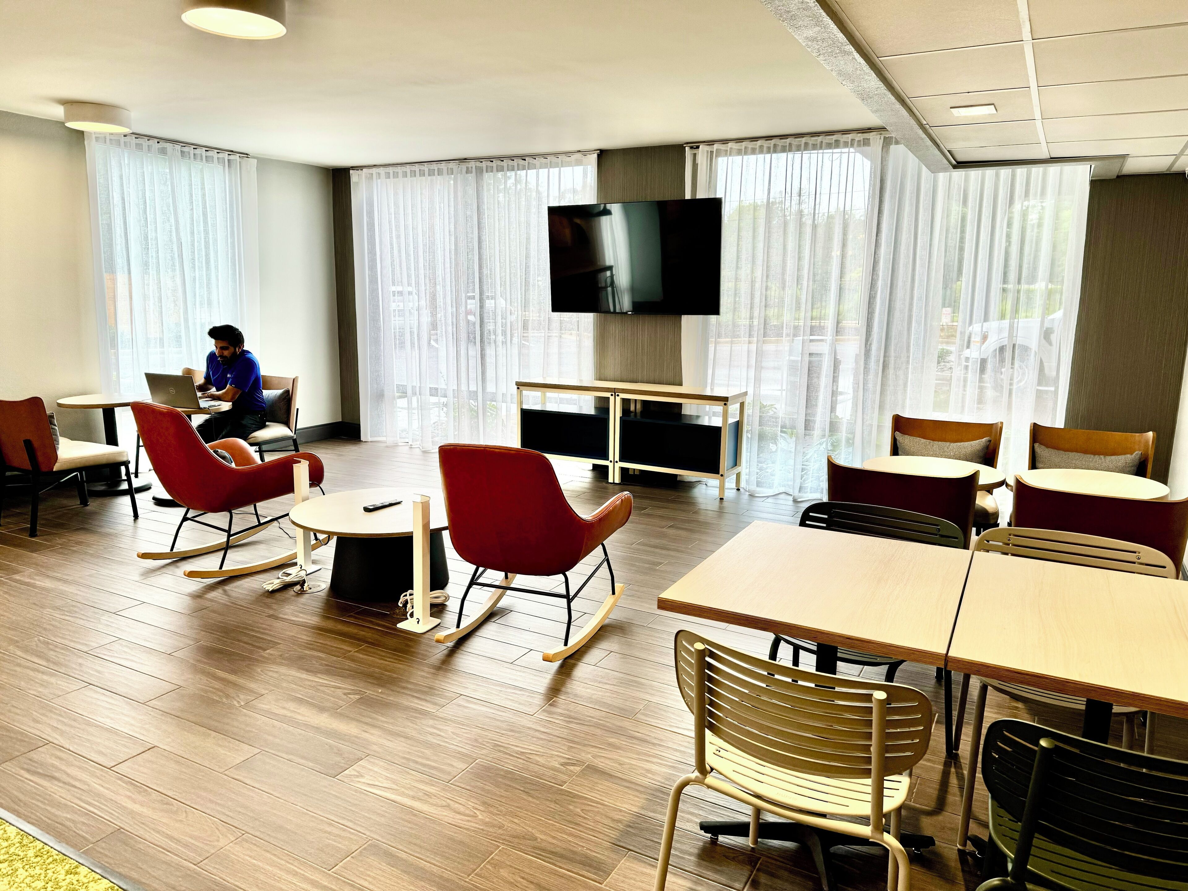 A modern hotel room with a flat-screen TV, comfortable seating, and large windows.