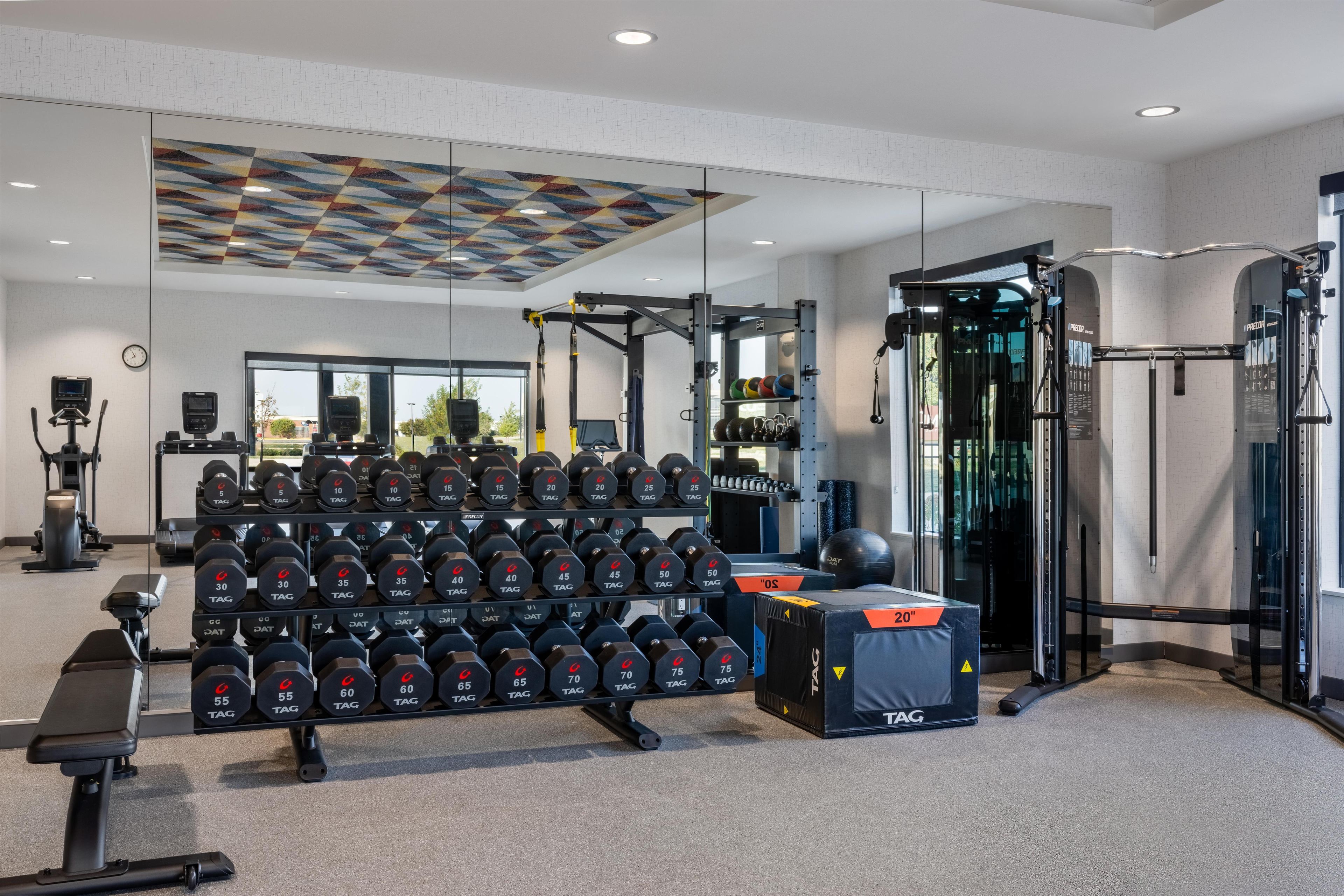 Ein Fitnessraum mit verschiedenen Trainingsgeräten, darunter Kurzhanteln, ein Squat-Gestell und eine Trainingsbank.