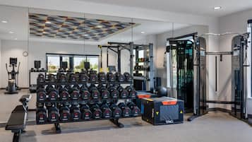 Ein Fitnessraum mit verschiedenen Trainingsgeräten, darunter Kurzhanteln, ein Squat-Gestell und eine Trainingsbank.