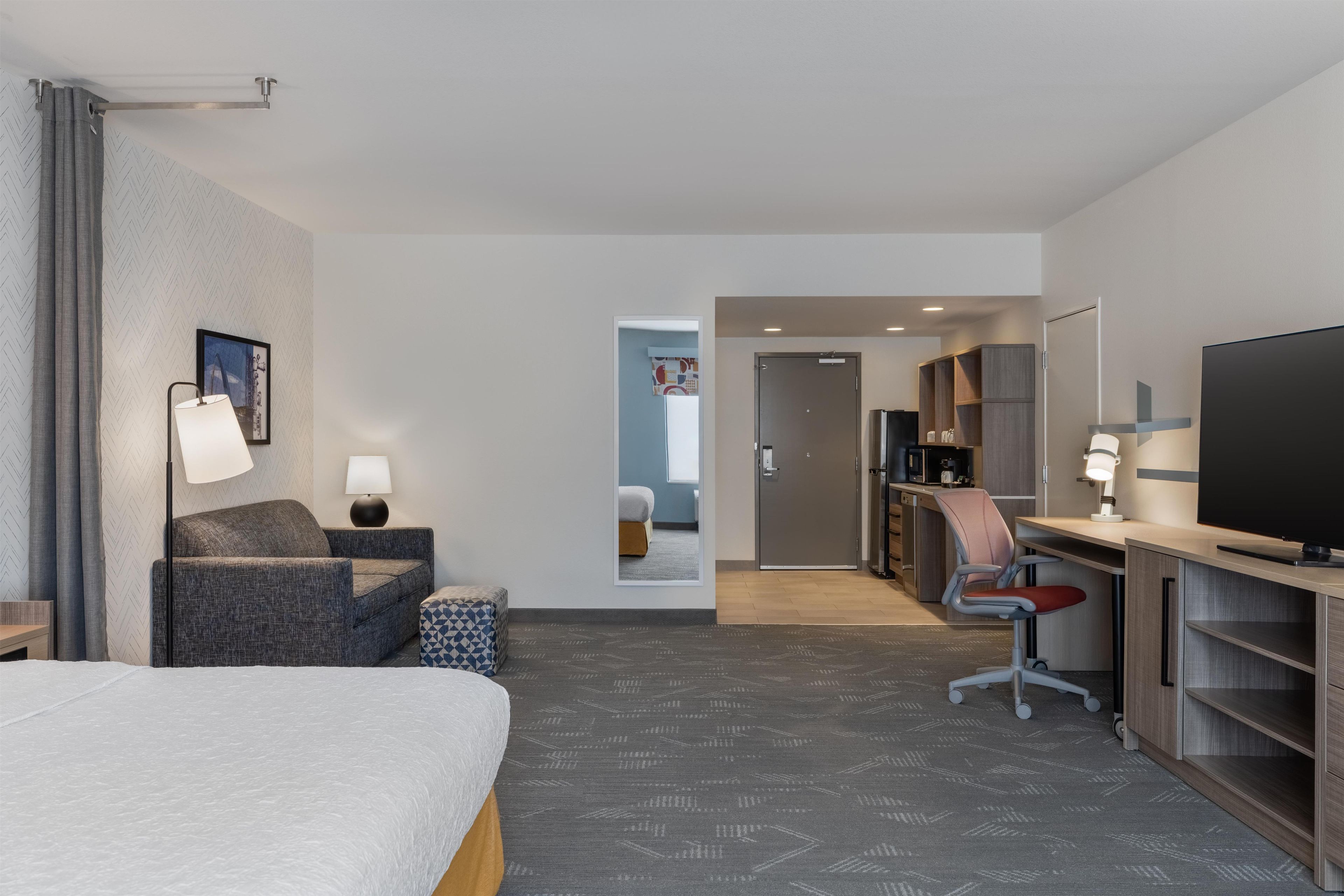 Ein Hotelzimmer mit Bett, Schreibtisch, Stuhl, Fernseher und einem durch eine geöffnete Tür einsehbarer Badezimmer.