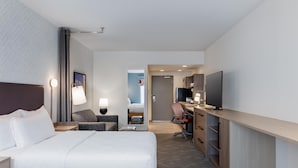 Ein Hotelzimmer mit Bett, Schreibtisch, Stuhl, Fernseher und einem durch eine offene Tür einsehbaren Badezimmer.