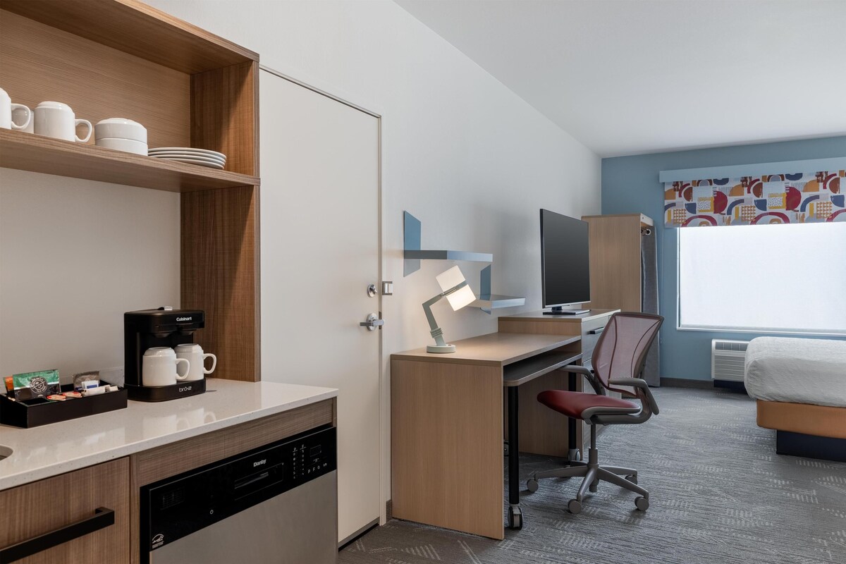 Una habitación de hotel con un escritorio de madera, una silla, una cama, un televisor y una cafetera.