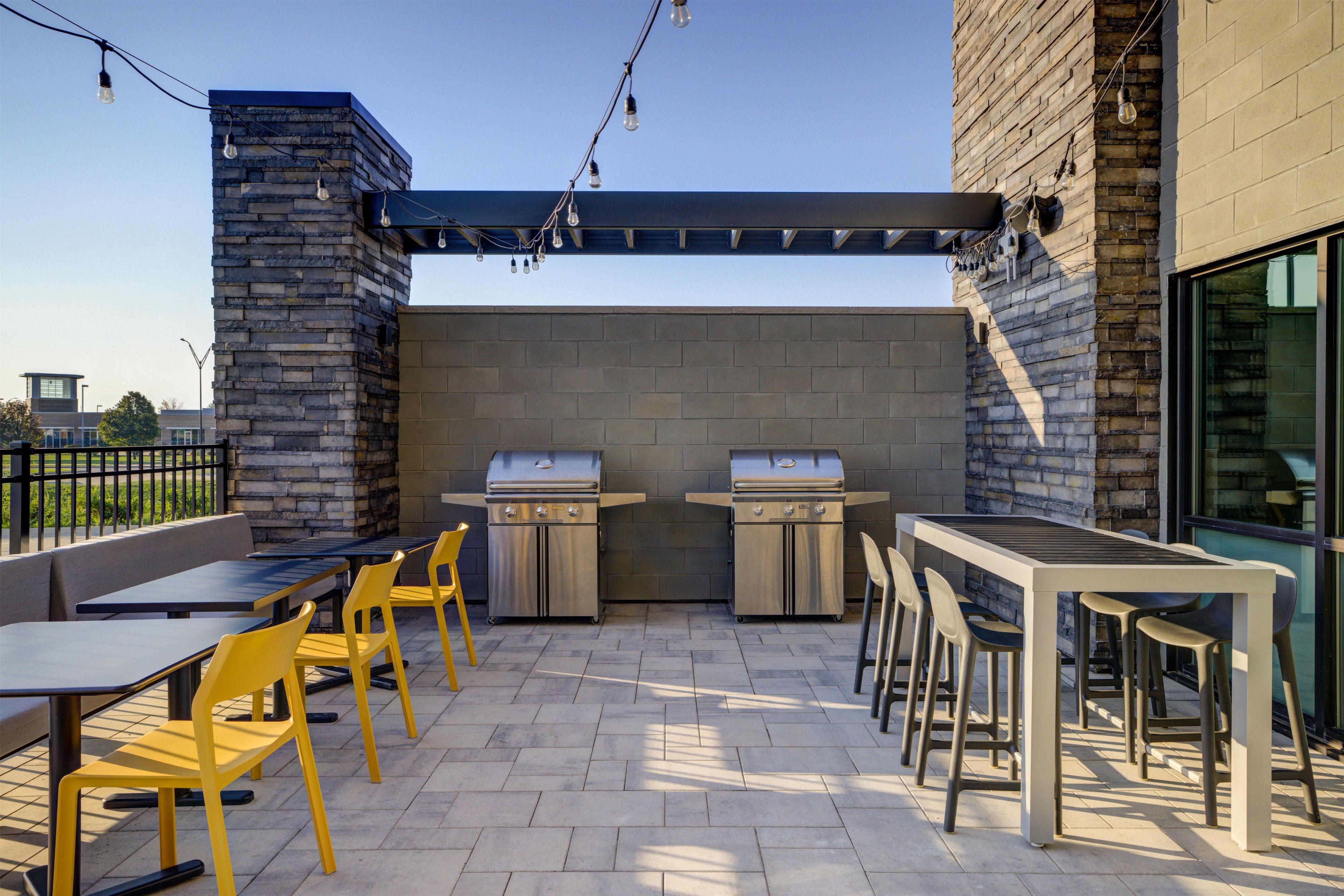 An outdoor patio with a grill, seating, and string lights.