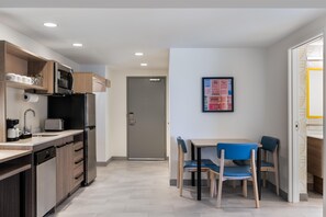 Een moderne keuken met inbouwapparatuur, een eethoek met een tafel en stoelen, en een deur naar een andere kamer.