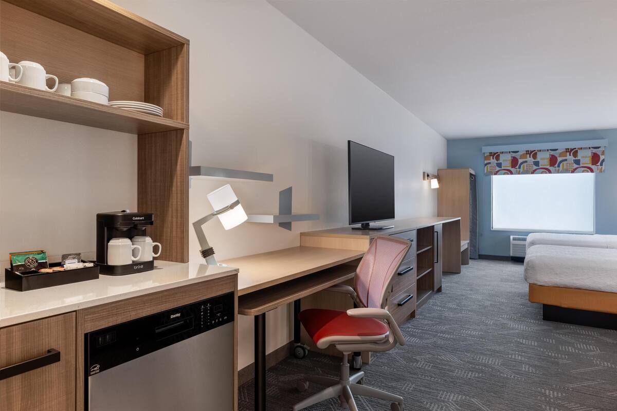 Een hotelkamer met een houten bureau, een televisie, een bed, een stoel en een raam met uitzicht.