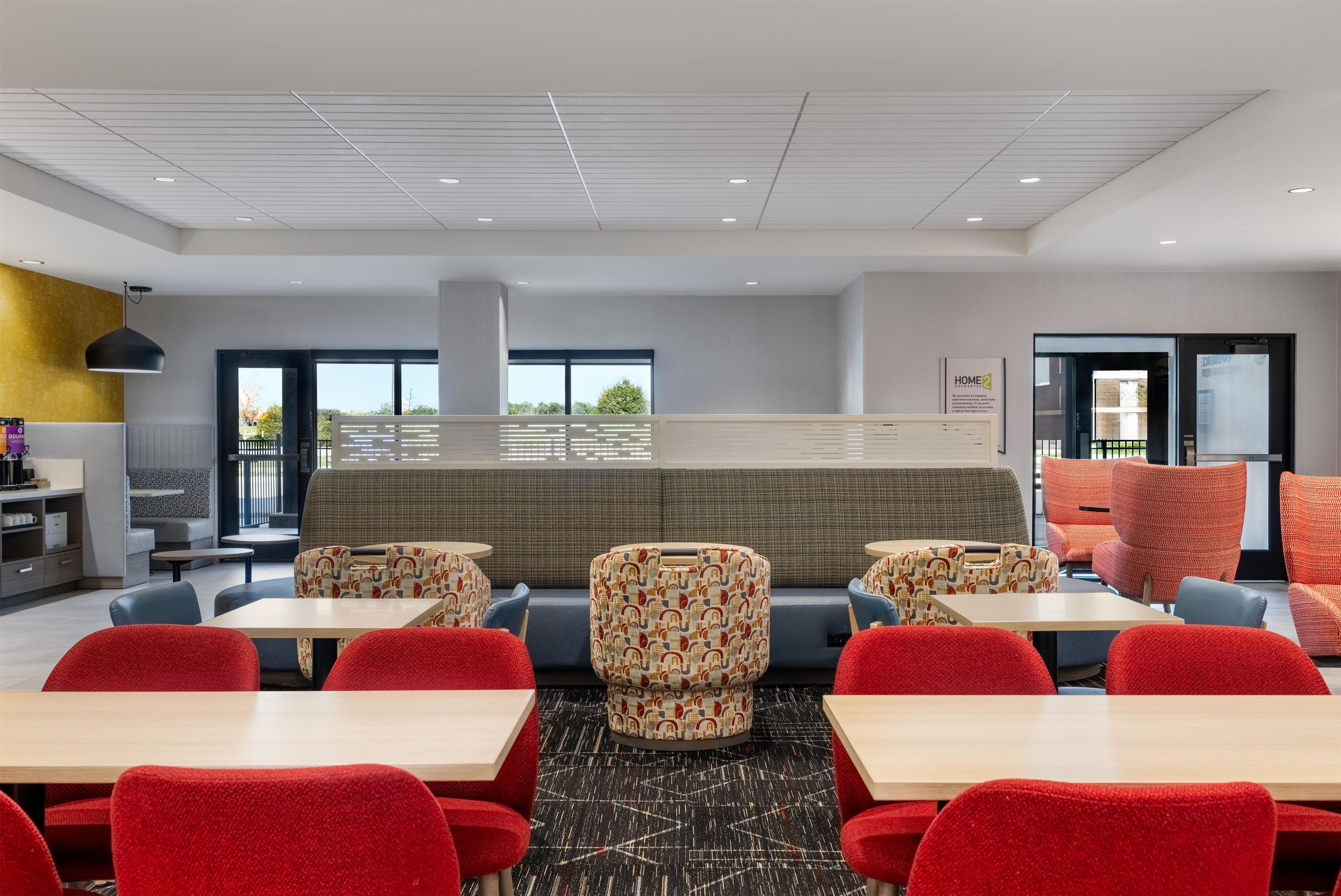 Un restaurant moderne avec des tables hautes et des chaises rouges, un banc à motifs et une vue sur l’extérieur.