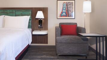 A hotel room with a bed, a desk, a chair, a nightstand, a lamp, and a framed picture on the wall.
