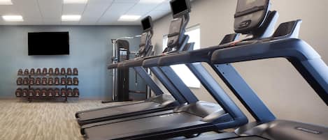 A gym with treadmills, dumbbells, and a TV screen.