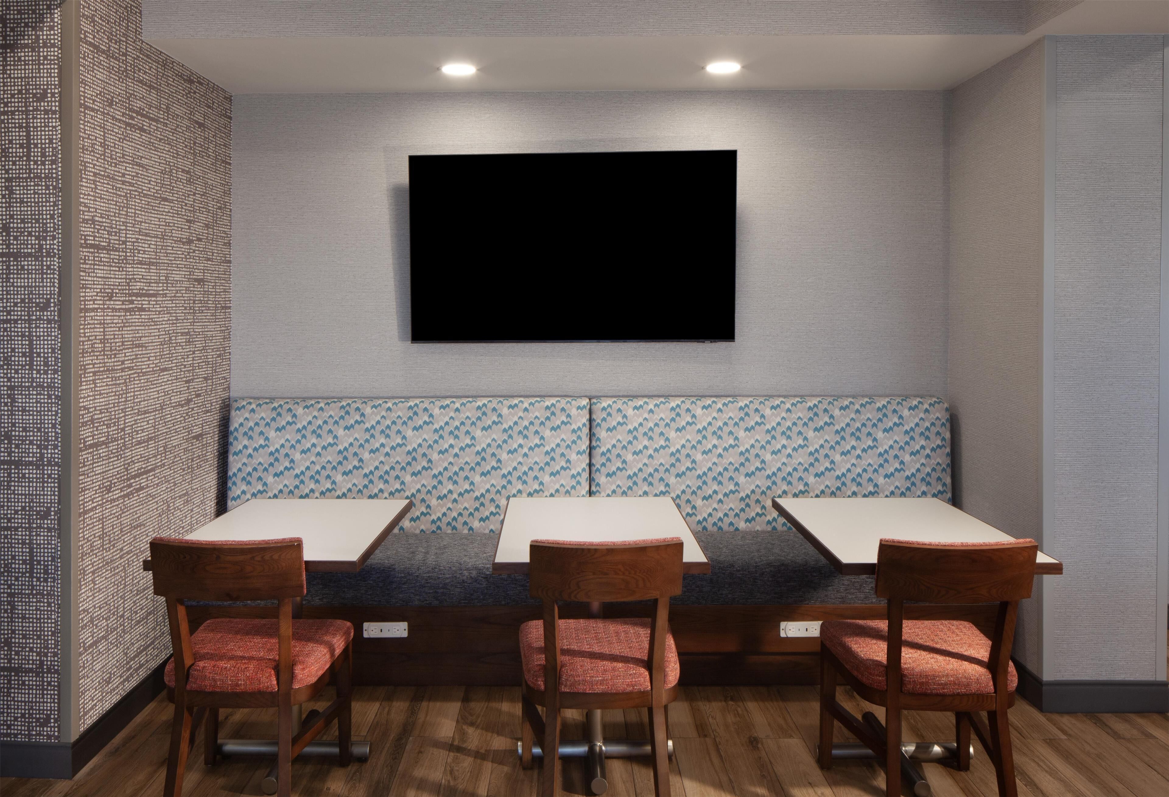 A restaurant with a large flat-screen TV mounted on the wall, wooden tables and chairs, and patterned wall designs.
