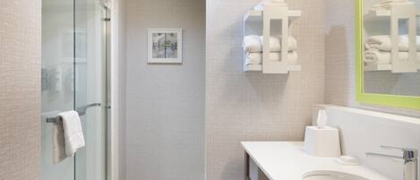 A modern bathroom with a glass shower, a white sink, and a mirror with a green frame.