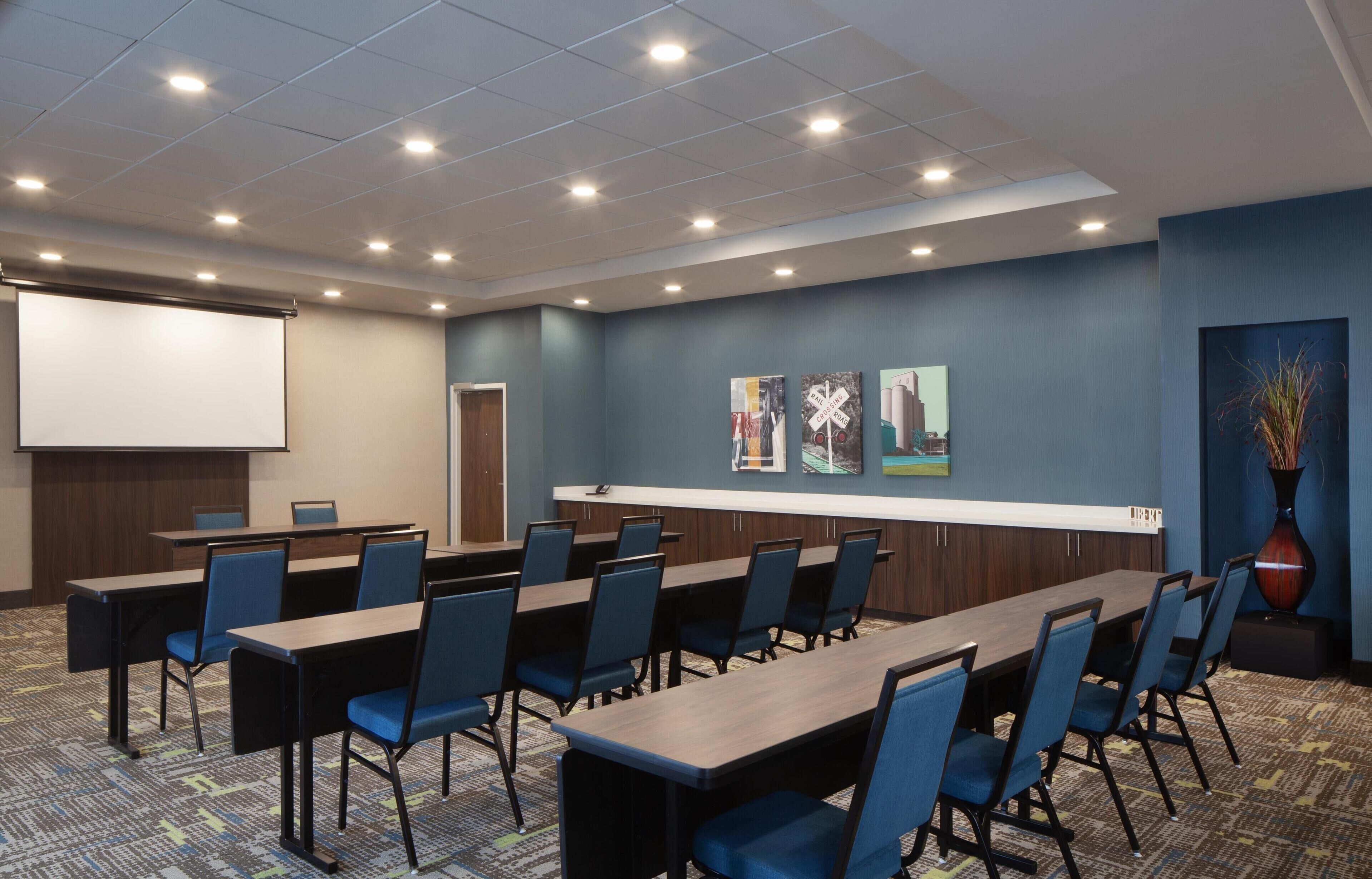 A conference room with a long table, chairs, a projector screen, and artwork on the walls.