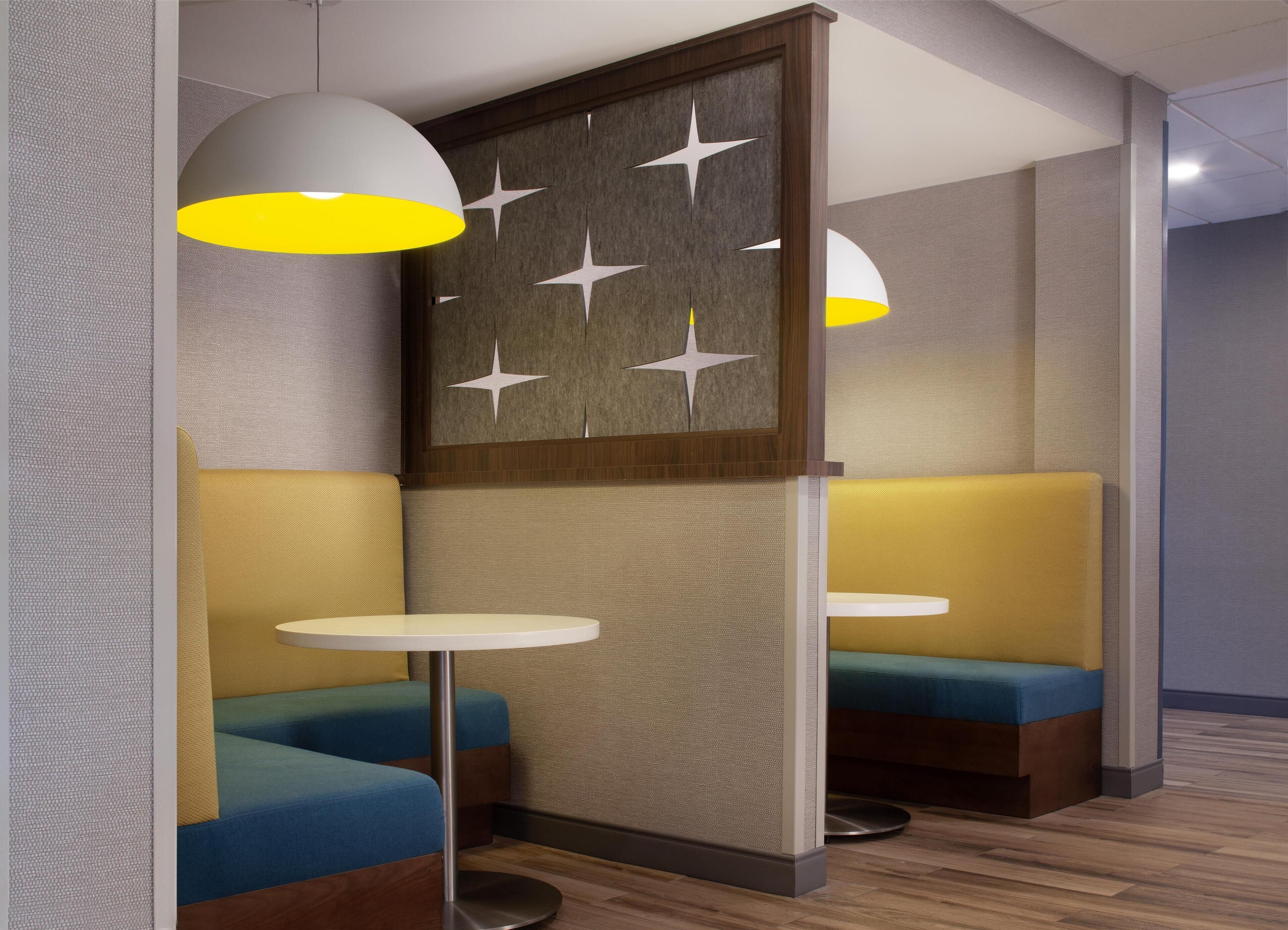 A modern seating area with cushioned benches and round tables, featuring a decorative wall panel with star cutouts.