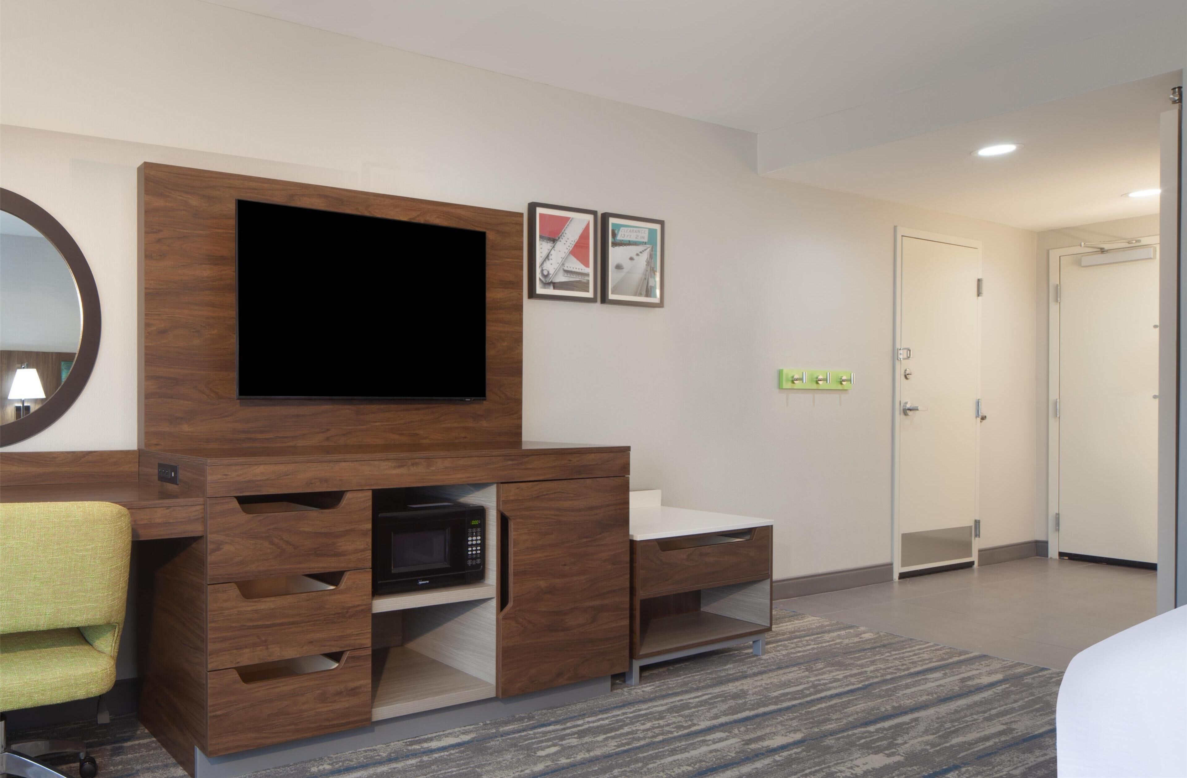 Hotelkamer met een houten bureau, een flatscreen televisie, een magnetron, een groene stoel en een deur naar de badkamer.
