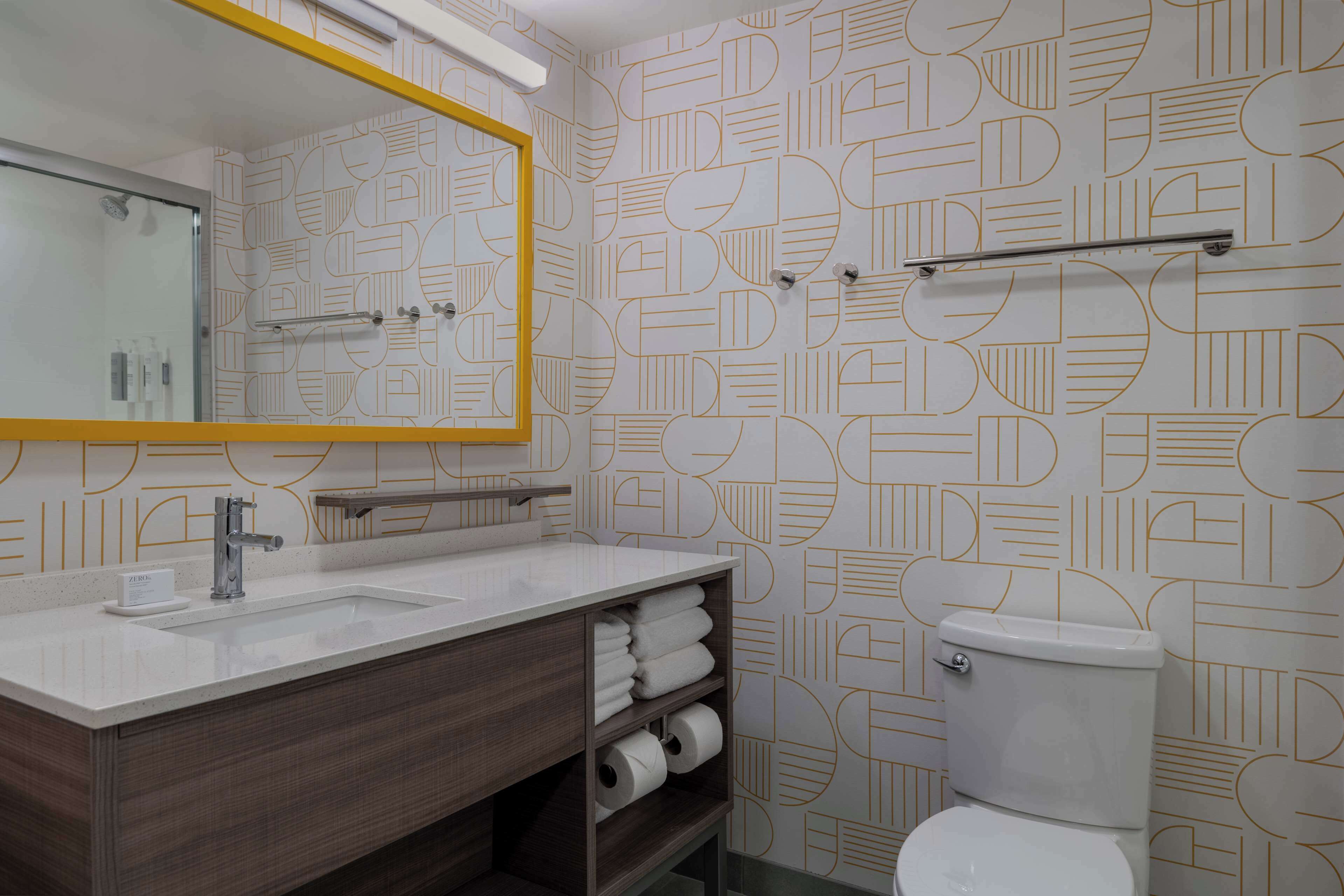 A bathroom with a geometric patterned wall, a white sink with a mirror, and a toilet.