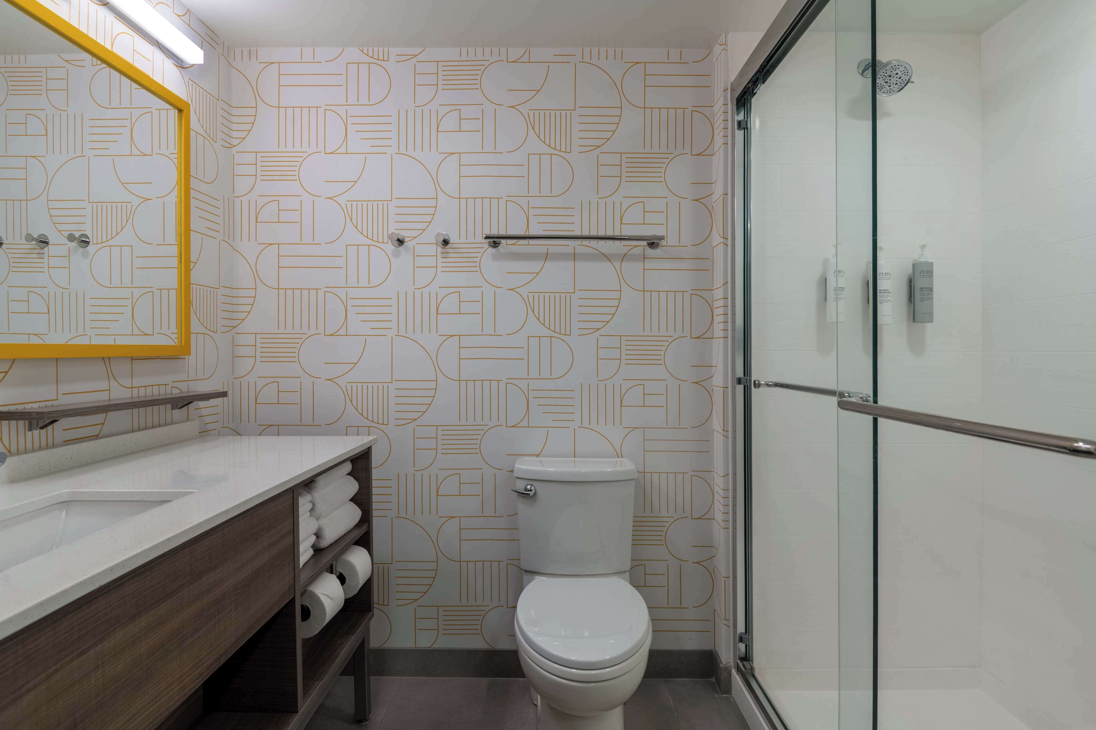 Ein Badezimmer im modernen Design mit Musterwand, Toilette, Duschkabine aus Glas und Waschtisch mit Spiegel.