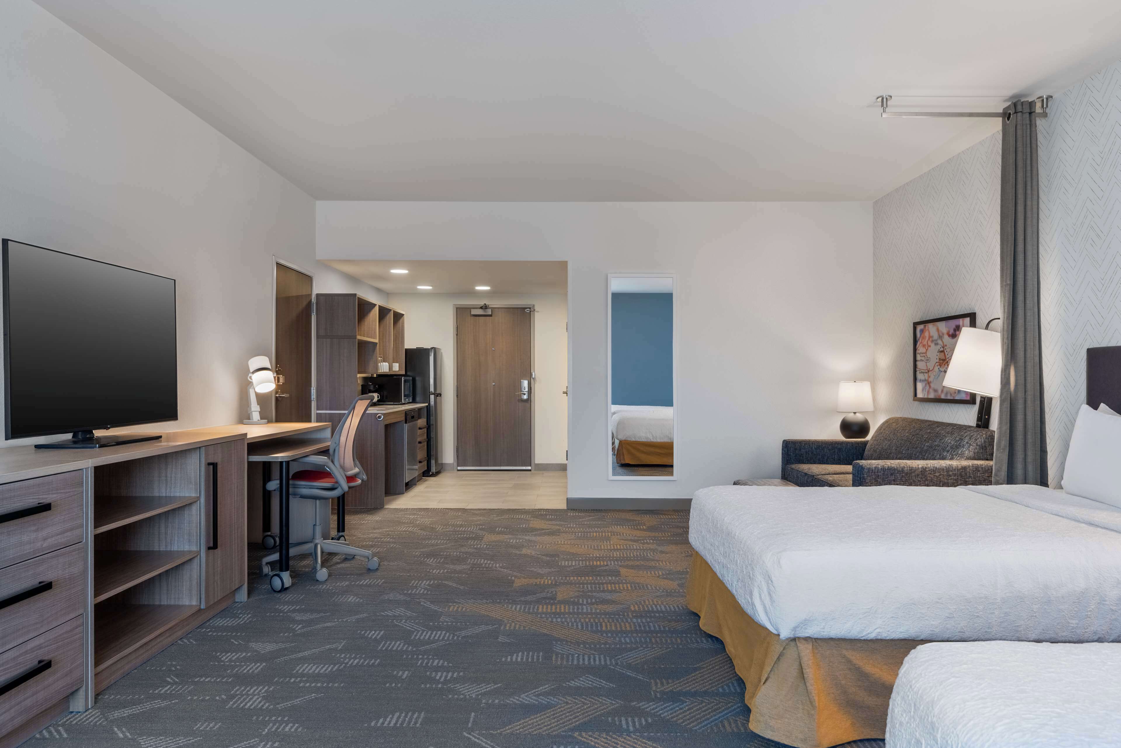 A hotel room with a large bed, a desk with a computer, a TV, and a wardrobe.