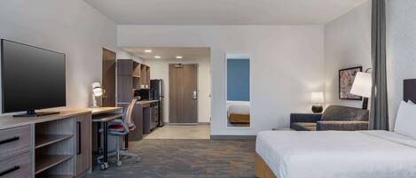 A hotel room with a large bed, a desk with a computer, a TV, and a wardrobe.