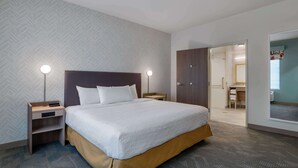 A hotel room with a large bed, two bedside tables with lamps, a wardrobe, and a bathroom visible through an open door. - Home2 Suites By Hilton Troy, Al (Troy)