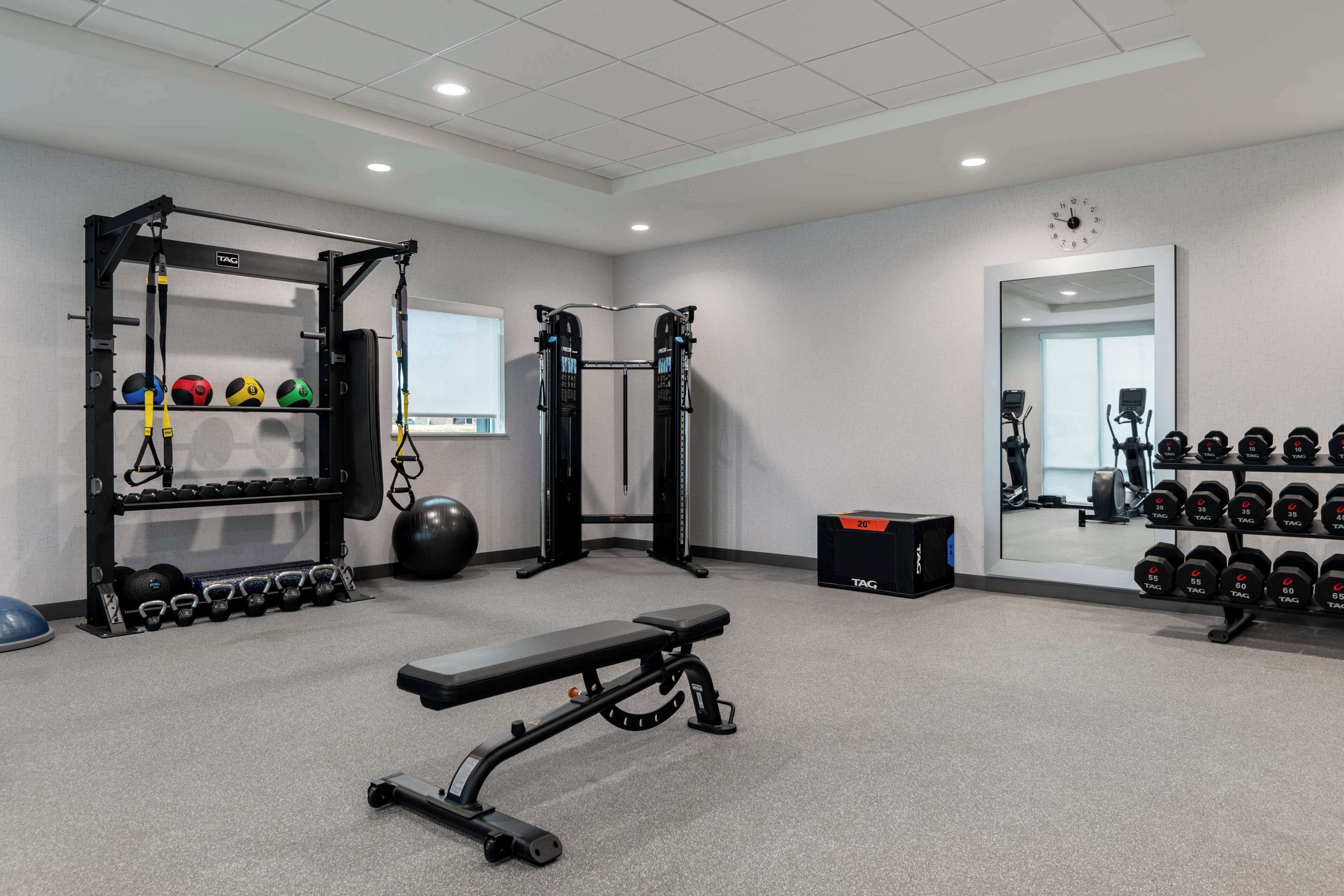 Ett gym med en stång för chins, en bänk och olika typer av vikter.