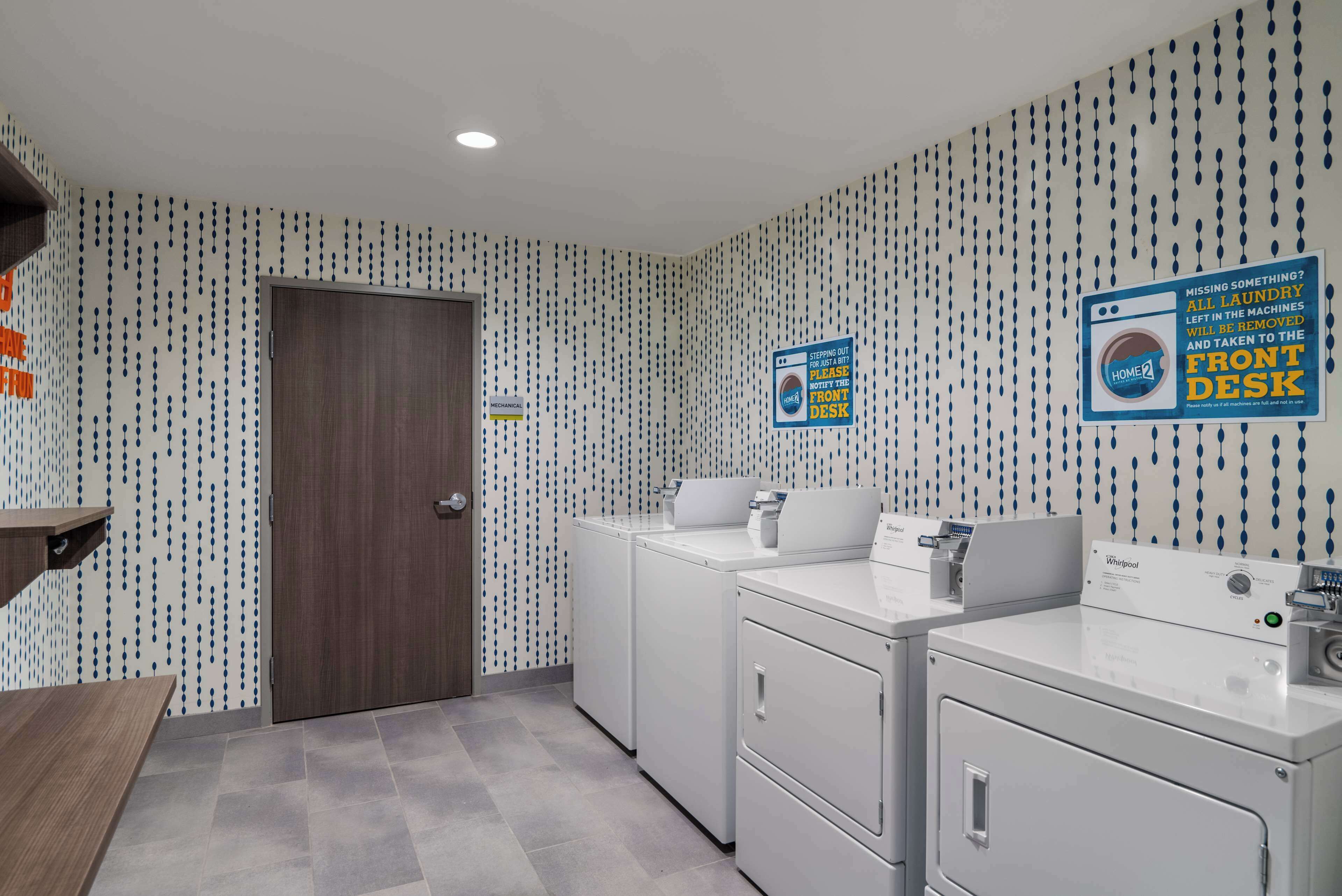 A laundry room with a door, two washing machines, and a sign indicating missing items should be reported to the front desk.