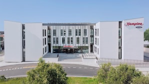 Un hotel moderno Hampton by Hilton con una fachada simétrica, amplias ventanas y una entrada destacada.