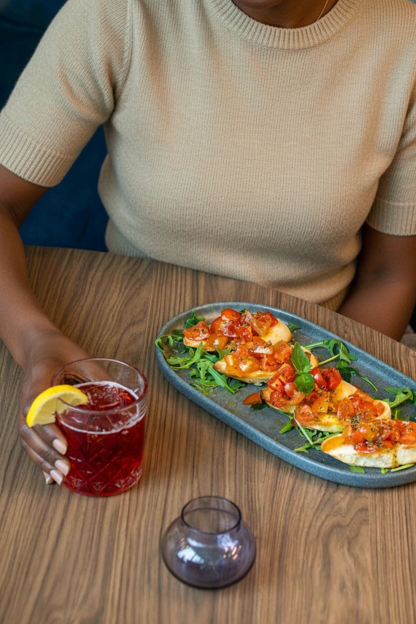 A person seated at a wooden table with a plate of food and a glass of red drink.
