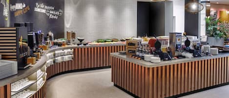 A modern breakfast bar with a curved design, featuring a variety of food items and a coffee station.
