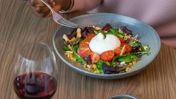 A person dining at a table with a bowl of salad, a glass of red wine, and a plate of cured meats.