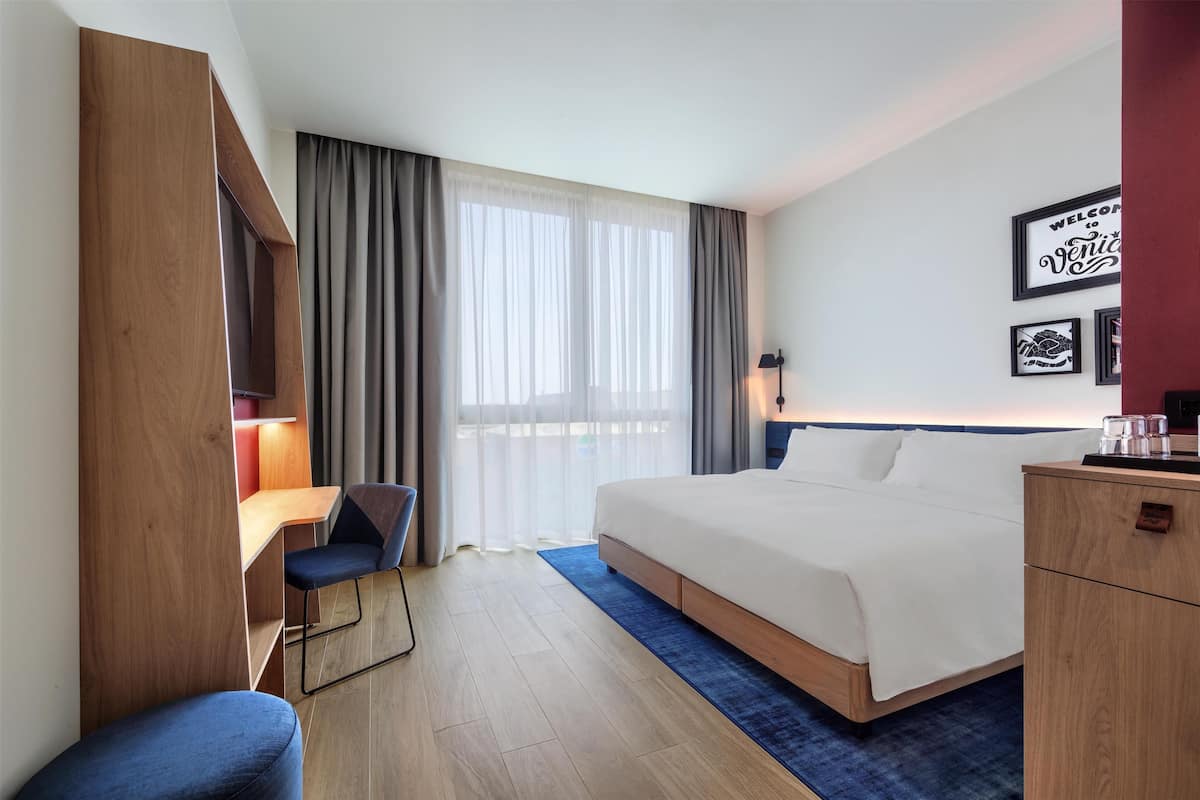 Una habitación de hotel con cama, escritorio, silla, armario y mesita de noche.