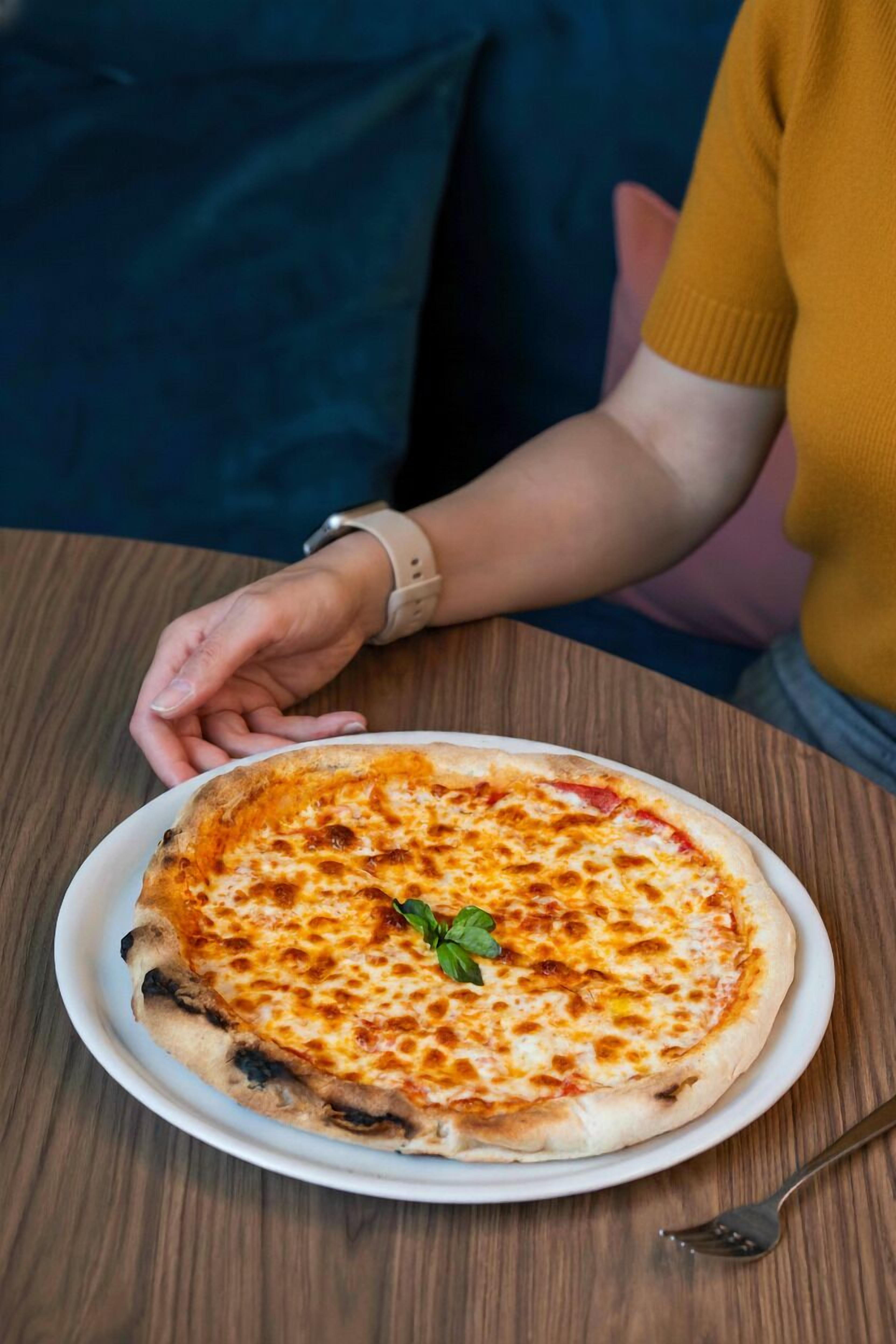 A person sitting at a wooden table with a pizza on a white plate.