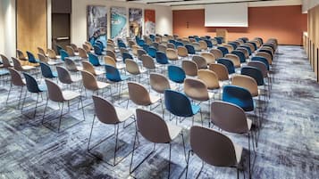 Ein Konferenzraum mit Reihen von Stühlen, einer Projektionsleinwand und einem großen Wandgemälde.