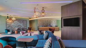 Un área de estar moderna con un amplio sofá modular, diversas opciones de asiento, un televisor de pantalla plana e iluminación ambiental.