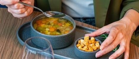 A person seated at a table with a bowl of soup, a glass of red wine, and a small dish of croutons.