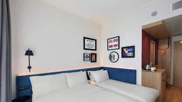 Quarto de hotel moderno com uma cama grande, uma mesinha, um abajur e obras de arte nas paredes.