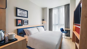 Habitación de hotel con cama, escritorio con silla, televisor y ventana con cortinas.