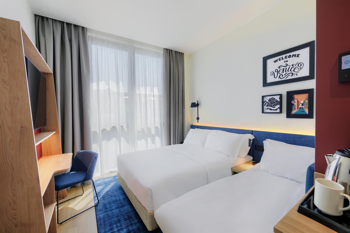 Une chambre d’hôtel avec deux lits, un bureau, une chaise et une machine à café.