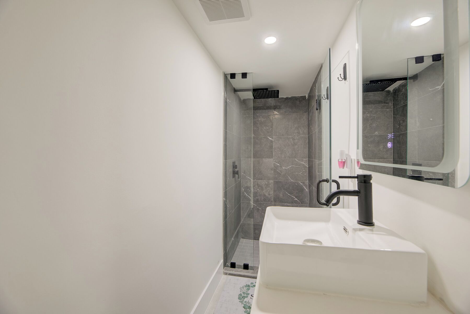 A modern bathroom with a white sink, a mirror, and a glass-enclosed shower area.