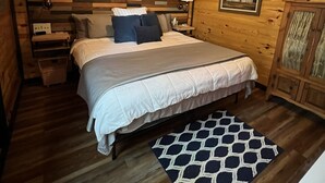 A wooden cabin bedroom with a bed, a ceiling fan, a nightstand, a lamp, a framed picture, and a cabinet.