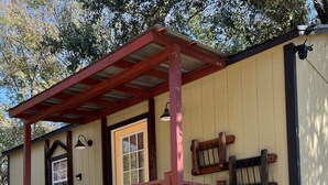 A small, single-story building with a porch, a door, and a sign that reads "Farmhouse". - Tiny Farmhouse Pickleball Court and Pet Friendly! (Granbury)