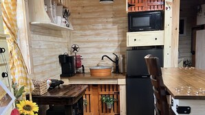 A rustic kitchen with wooden walls, a black refrigerator, a wooden table, and a hanging light fixture. - Tiny Farmhouse Pickleball Court and Pet Friendly! (Granbury)