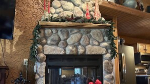 A stone fireplace with a Christmas wreath and candles, a television mounted on the wall, and a kitchen area in the background. - Great family retreat! Pickleball  and pet friendly (Granbury)
